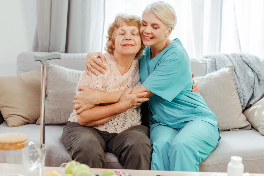 nurse hugging elderly woman on sofa at home